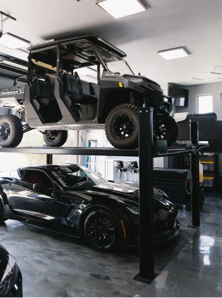 Bright garage lighting above a car lift and two parked vehicles
