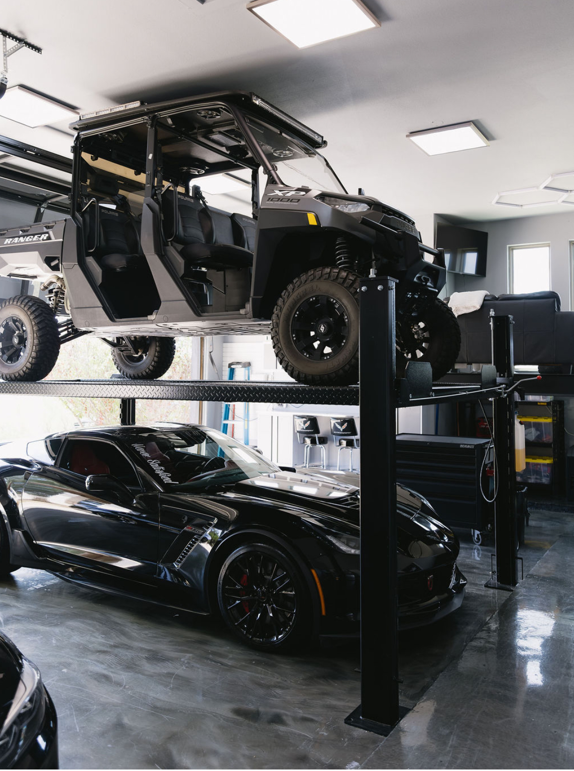 Bright garage lighting above a car lift and two parked vehicles