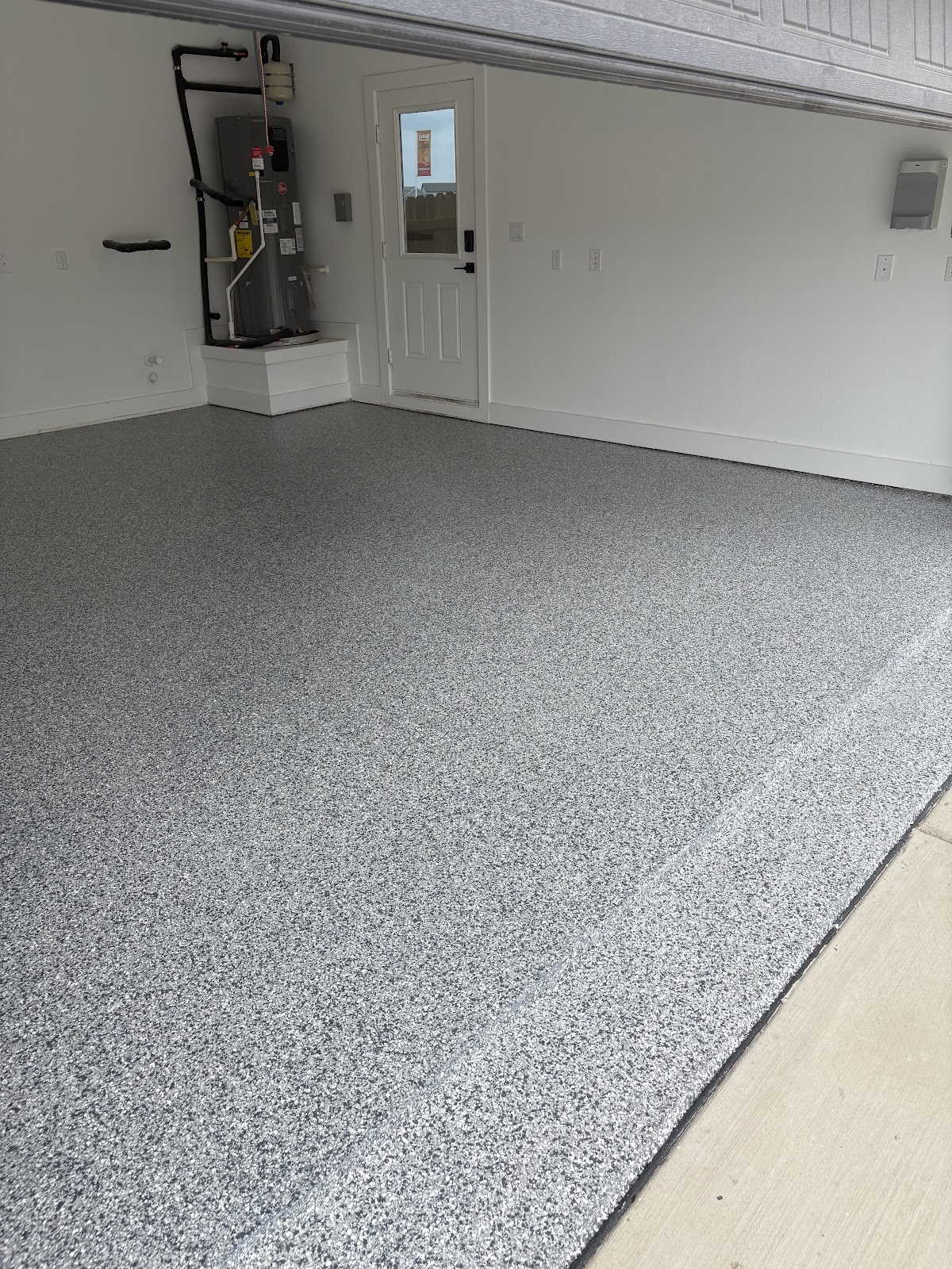 Finished gray flake garage floor beside a utility wall